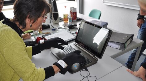 Frau an Laptop mit Rheumahandschuhen