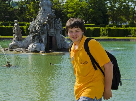 Junge mit Rucksack vor Brunnen